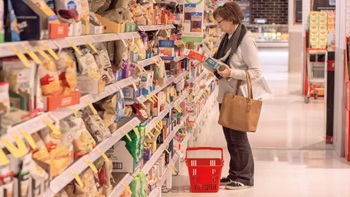 Signora di fronte agli scaffali del supermercato con in mano una confezione